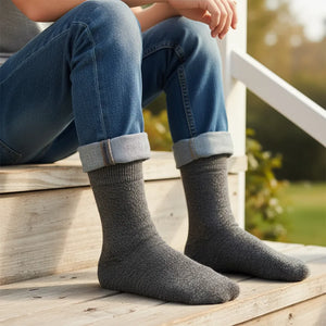 Person wearing grey boot socks and blue jeans sitting on a wooden bench outdoors.