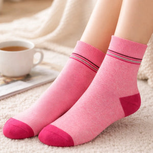 Pink socks with striped cuffs worn by a person, with a cup of coffee in the background.